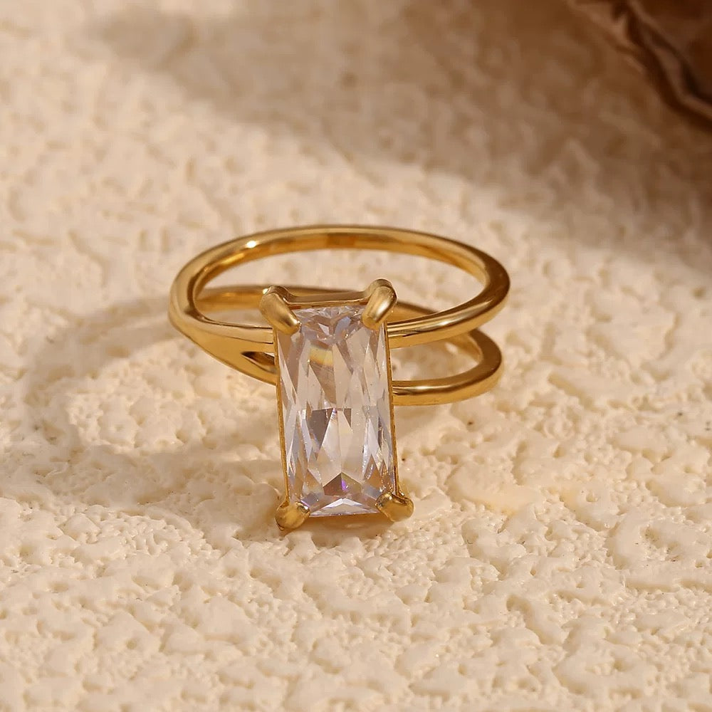 Gold ring with a rectangular gemstone on a textured beige surface