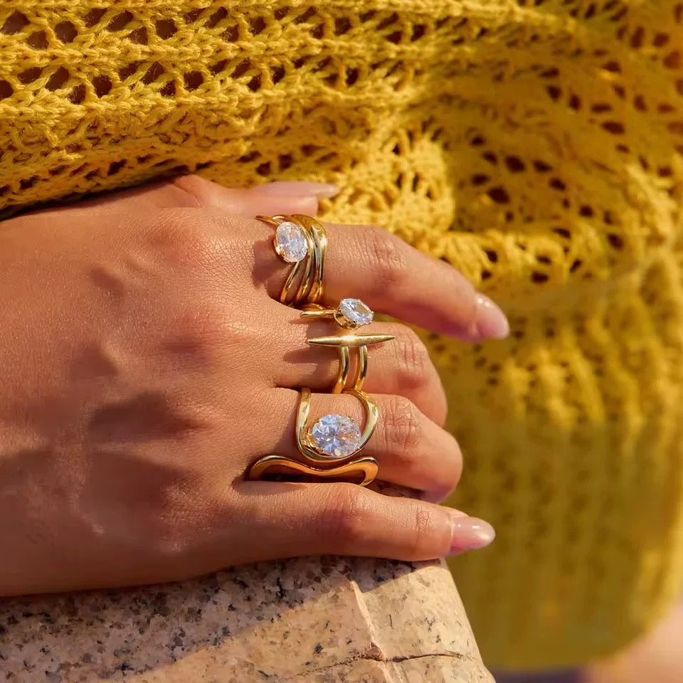 Hand wearing gold rings with clear stones against a yellow textured background