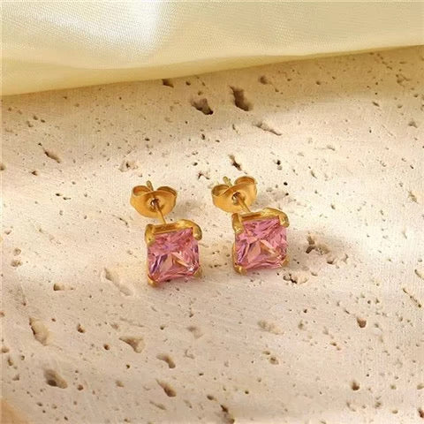 Gold earrings with pink gemstones on a textured beige surface