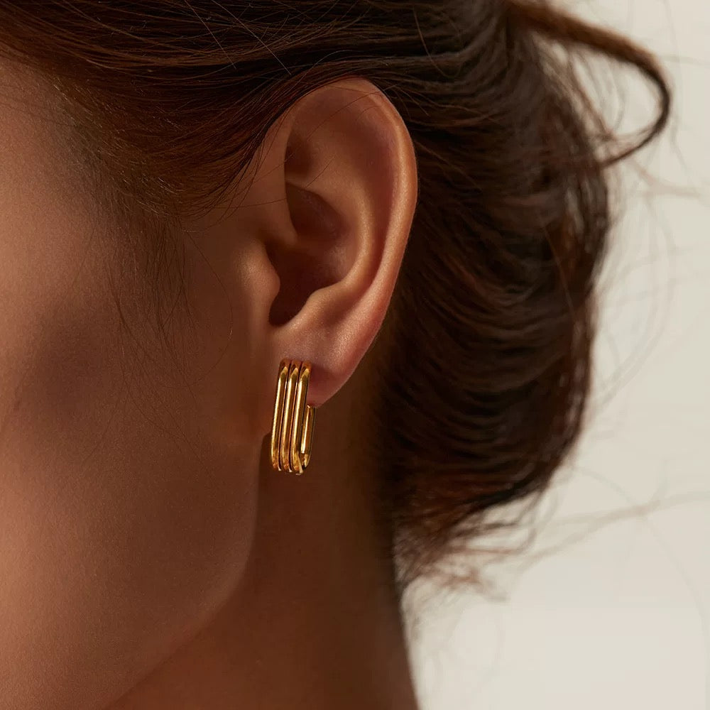 Close-up of an ear wearing gold hoop earrings with a neutral background