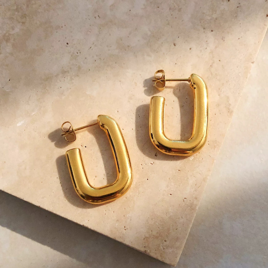 Gold hoop earrings on a beige stone surface