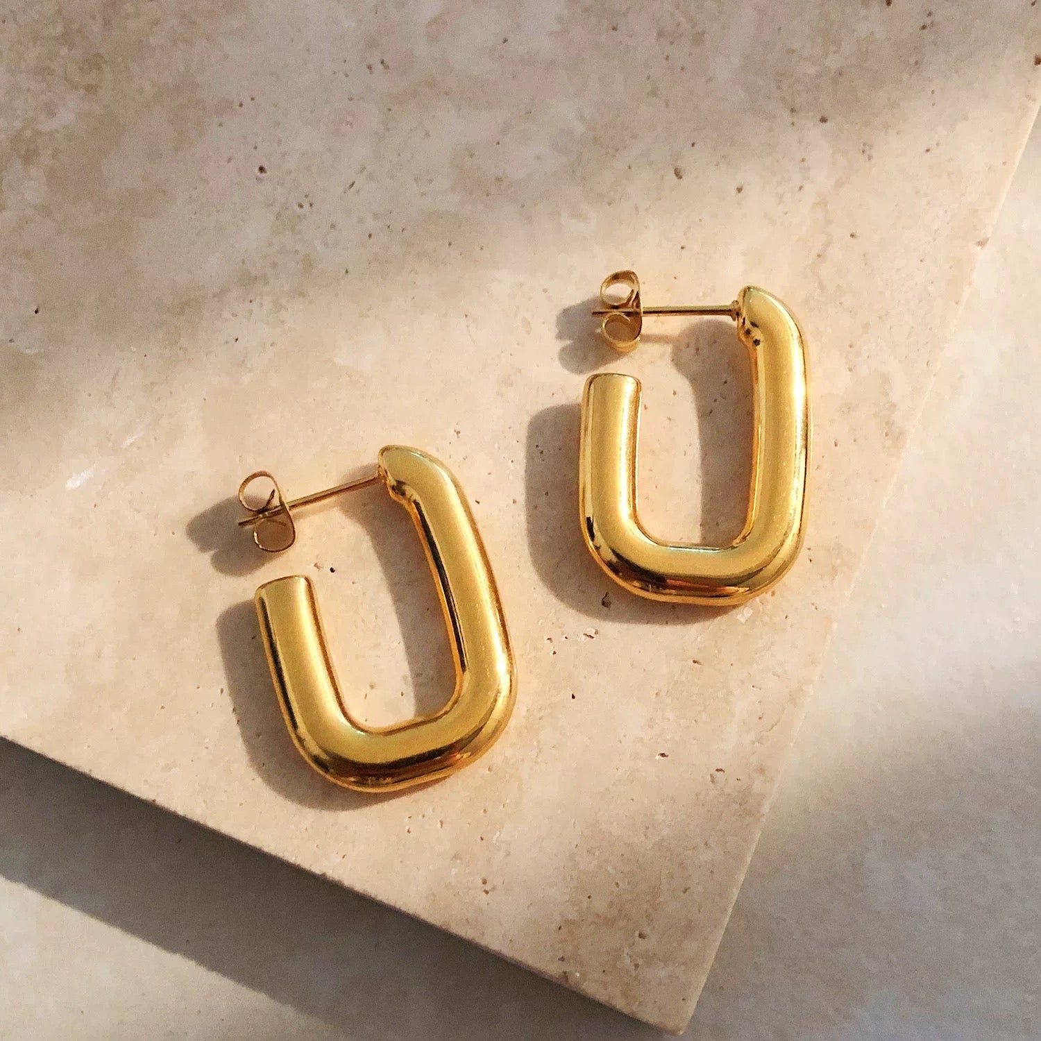 Gold hoop earrings on a beige stone surface