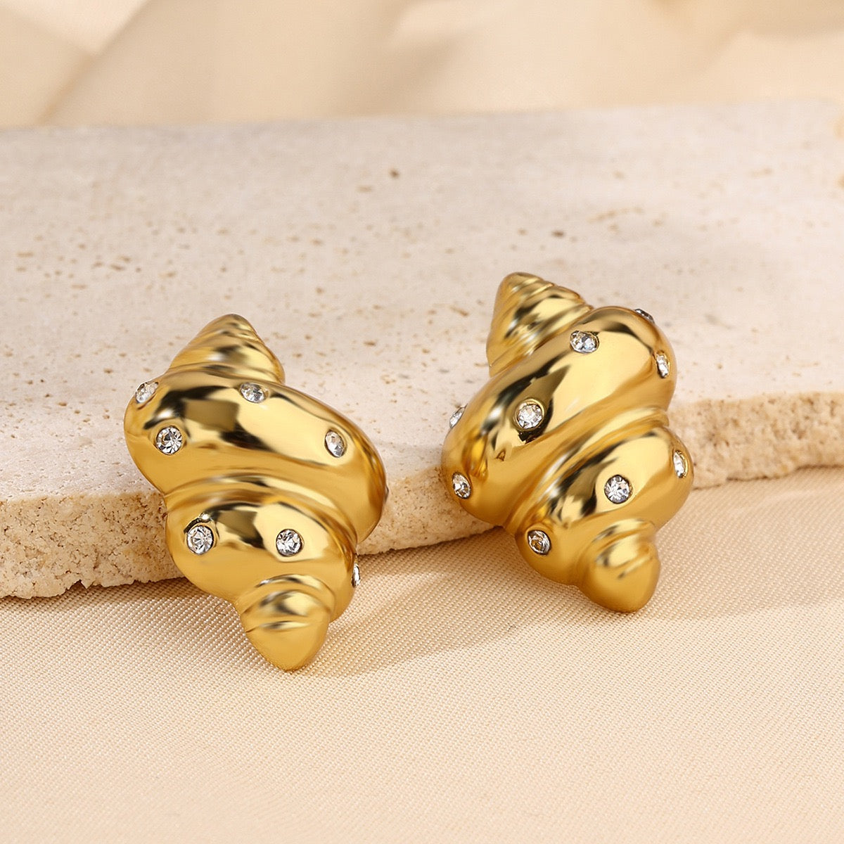 Gold shell-shaped earrings with embedded stones on a beige fabric background