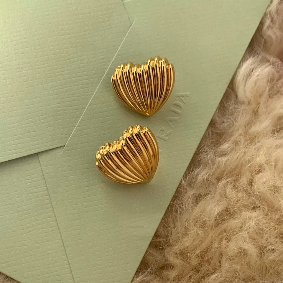 Gold heart-shaped earrings on a textured green surface