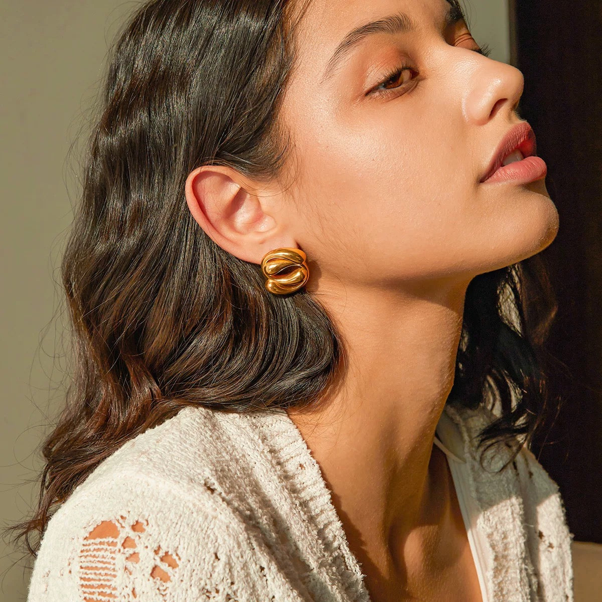 Close-up of a woman wearing gold earrings with a neutral background