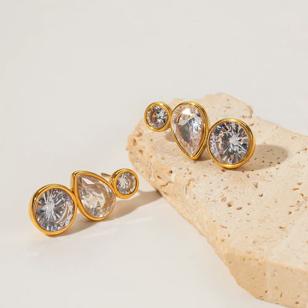 Gold earrings with clear gemstones on a beige stone background