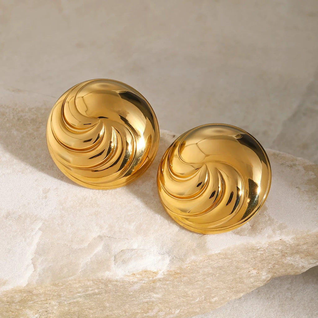 Pair of gold spiral earrings on a textured beige surface