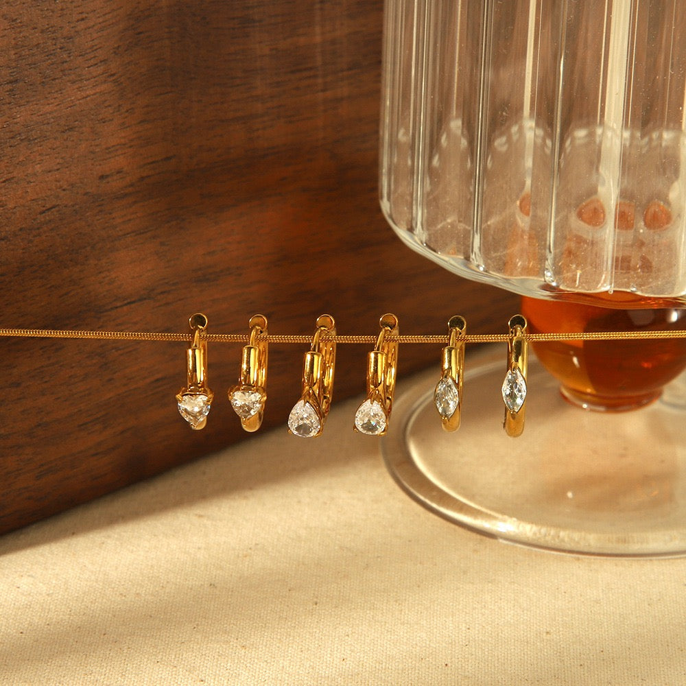 Gold earrings with clear stones on a string, placed on a glass surface with a wooden background.