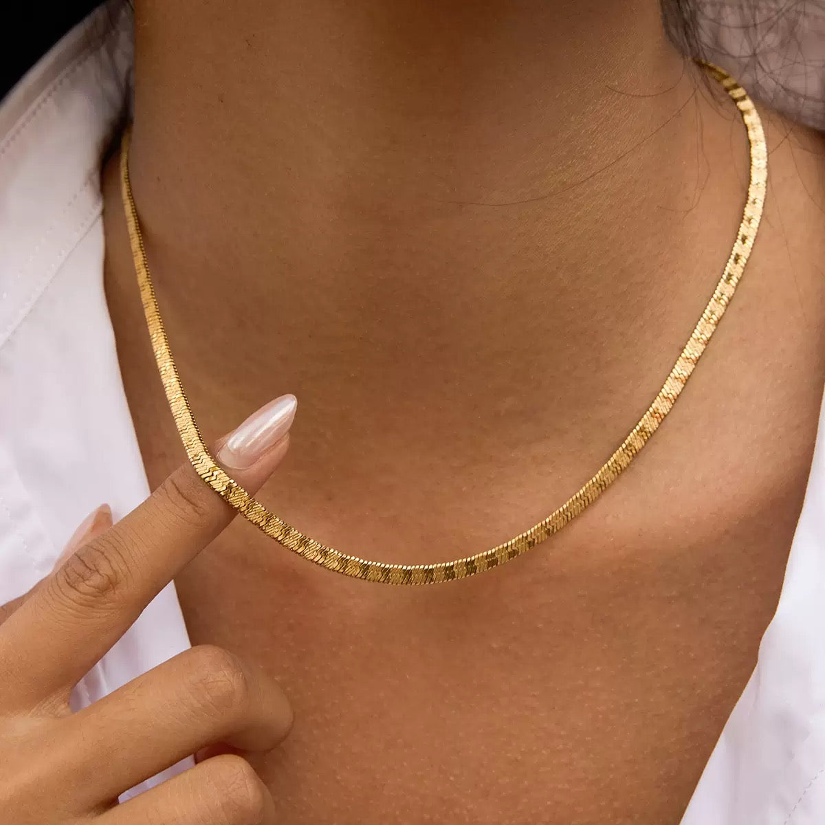 Gold necklace being worn on a person's neck with a white shirt.