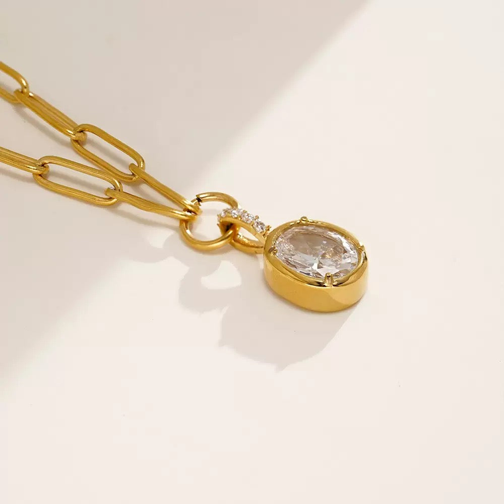 Gold necklace with a pendant featuring a clear gemstone on a light background