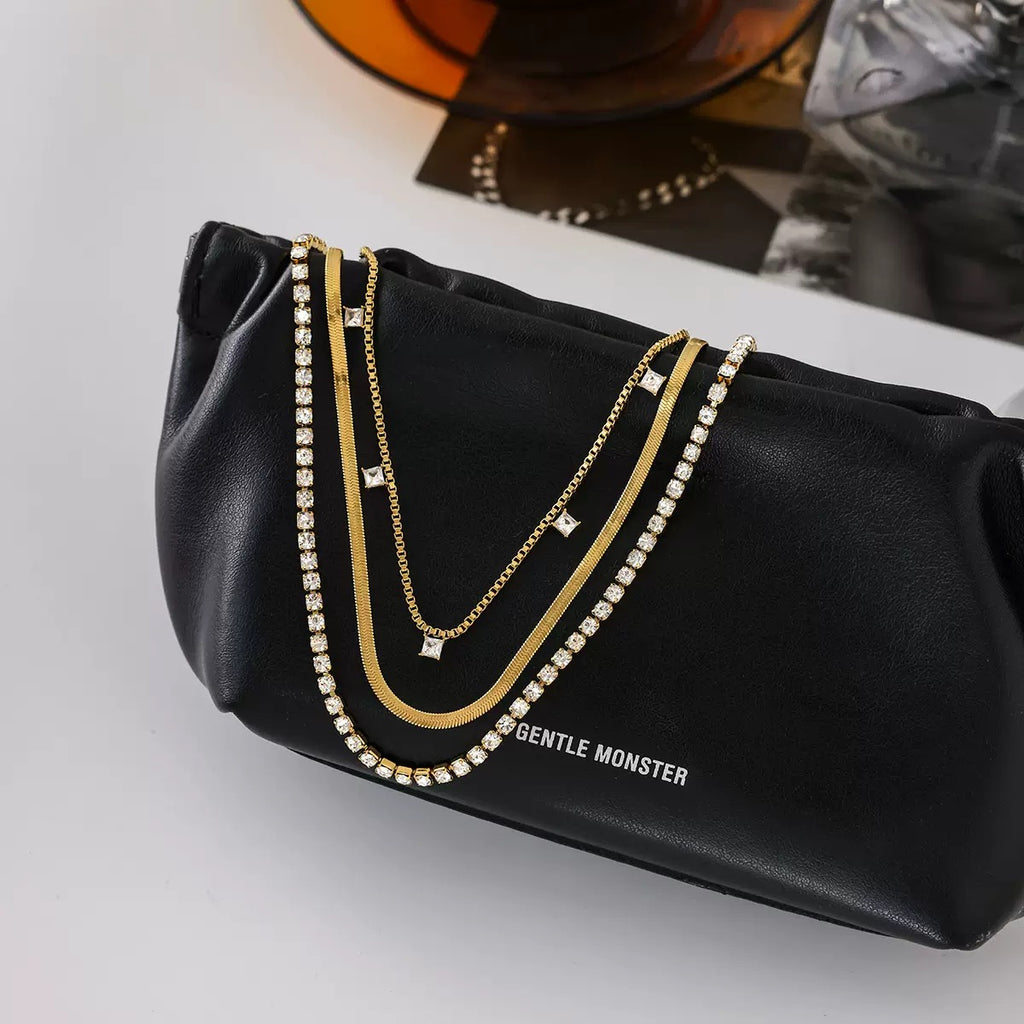 Black clutch bag with gold chain and 'Gentle Monster' branding on a light gray background