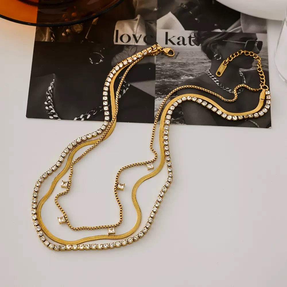 Gold necklace with rhinestones on a white surface with a magazine in the background