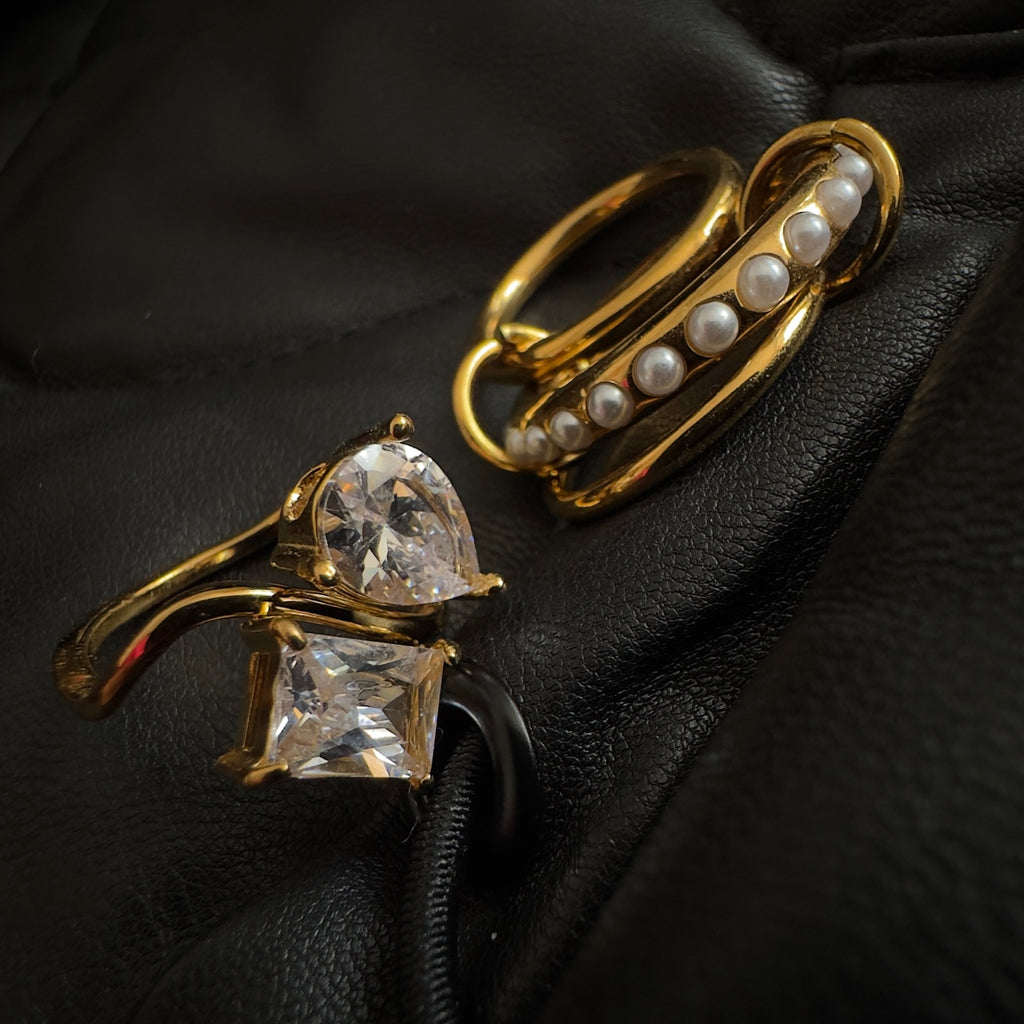 Gold rings with gemstones and pearls on a black textured surface