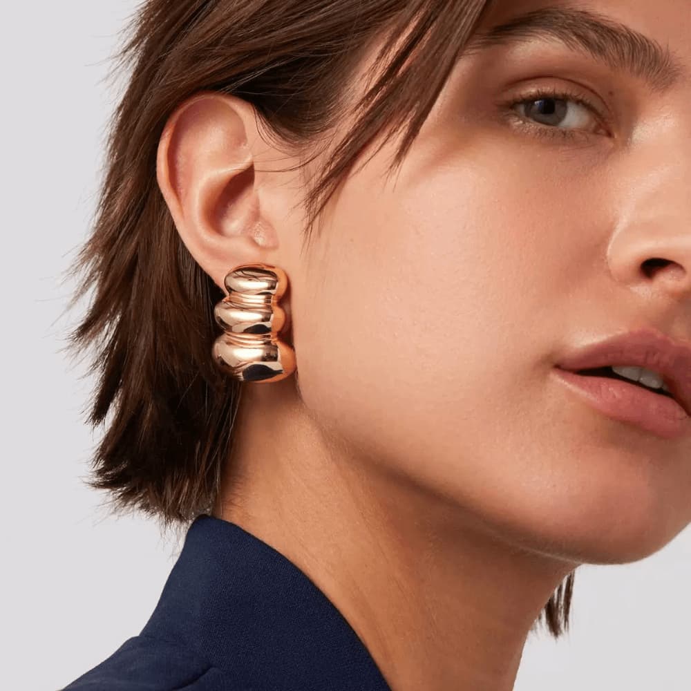 Close-up of a person wearing gold hoop earrings with a neutral background
